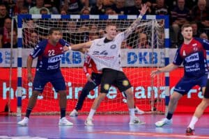 Linus Arnesson steht am Kreis, die eine Hand den Ball fordernd in die Höhe gestreckt. Ein Abwehrspieler aus Flensburg zieht ihm dabei leicht von der Seite am Trikot.